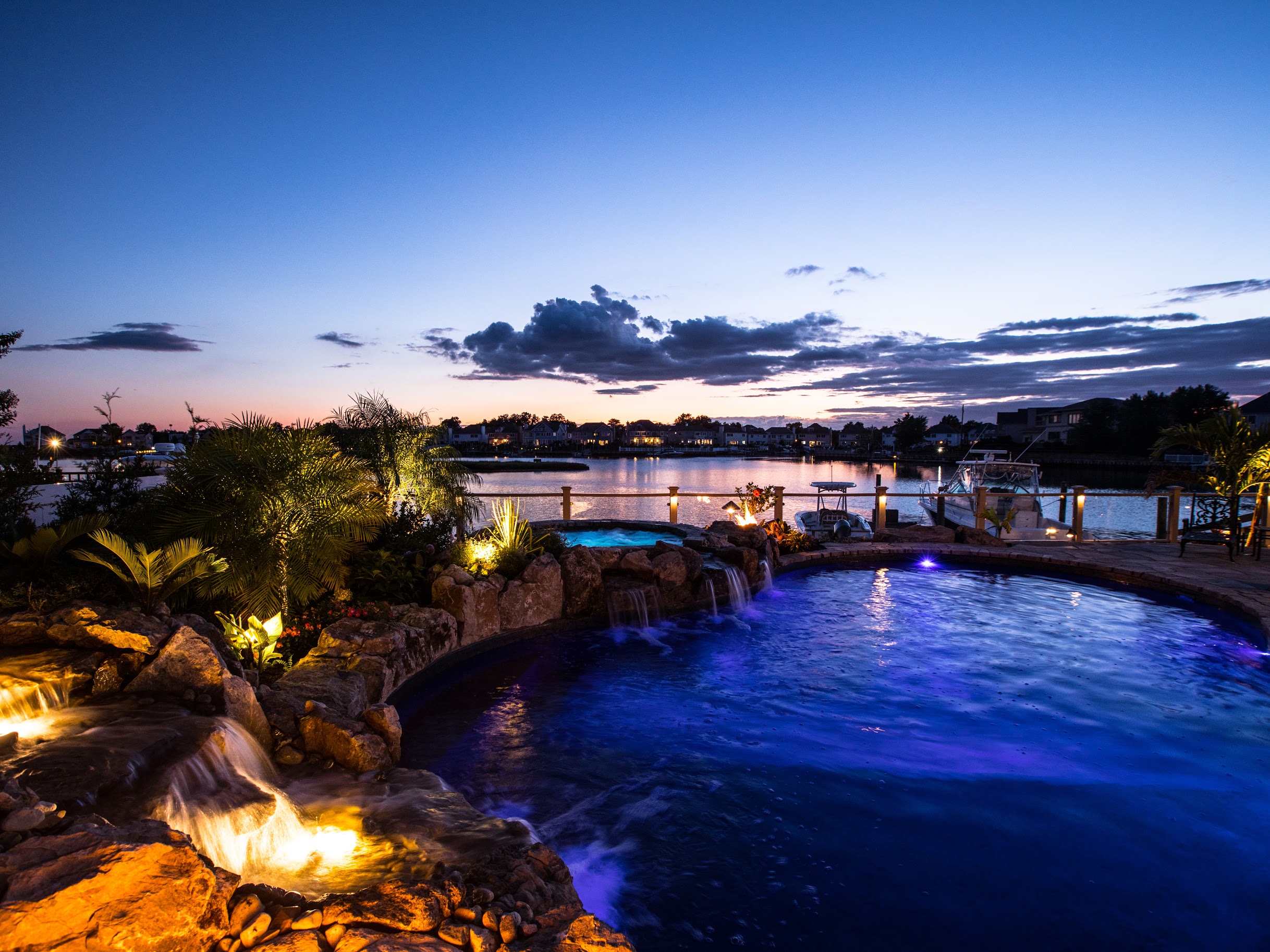Waterfront swimming pool with illuminated waterfall at dusk